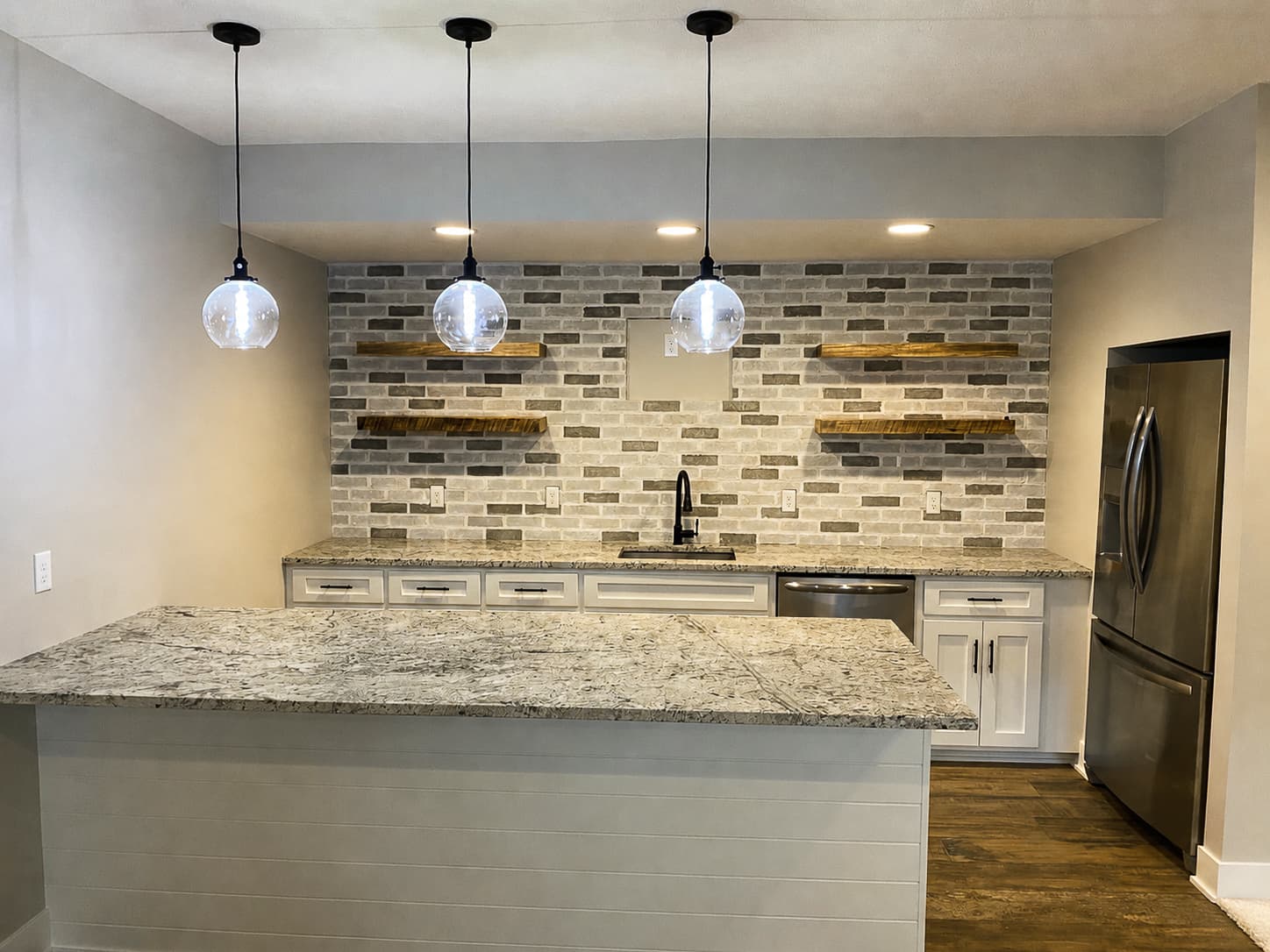 Basement wet bar with brick backsplash, floating wood shelves, and granite counters