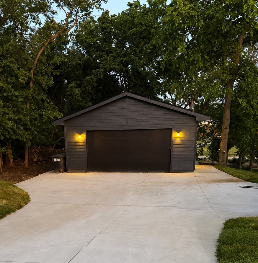 Dark stained detached two-car garage with wall sconces at dusk